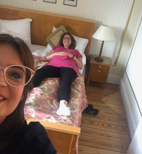 Anna Blomberg ligger i sin hotellsäng på Grand Hotel. Susanna Dzamic står i förgrunden och tar "selfie"